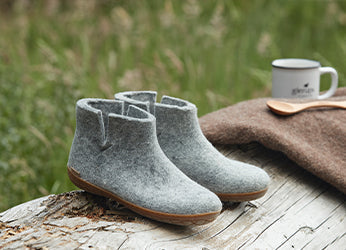 A pair of Grey glerups boots placed on a wooden surface outdoors, with a brown blanket and a cup in the background.