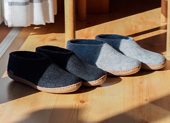 Two pairs of glerups shoes in the color Charcoal grey and Grey placed on a wooden shelf indoors, each with a natural calfskin leather sole.