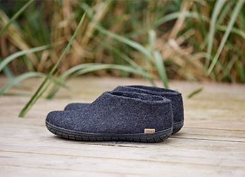 A pair of Charcoal grey glerups shoes placed on a wooden deck with tall green grass in the background. The shoes have a black rubber sole.