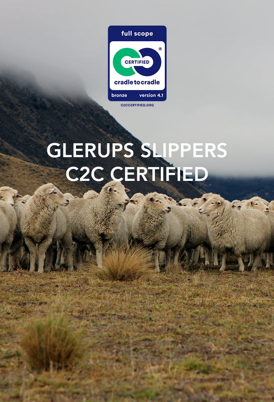 A large flock of sheep standing on grassy terrain with mountains in the background under an overcast sky. A Cradle to Cradle certification logo is displayed in the upper right corner.