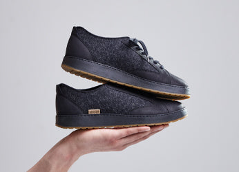 A pair of Charcoal grey glerups langdal shoes with rubber soles is displayed stacked on a hand against a light background.