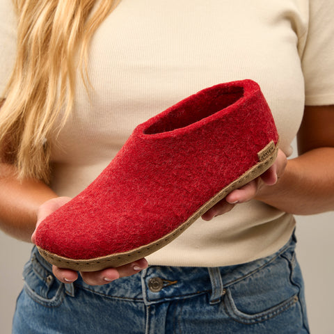 Close-up picture of a person holding a Red glerups shoe with a leather sole.