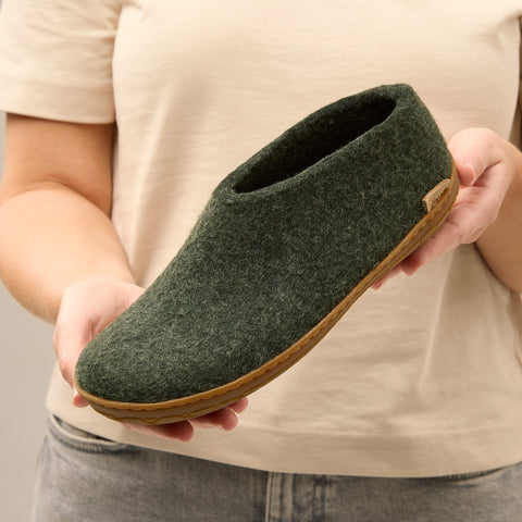 Close-up picture of a person holding a Forest green glerups shoe with a natural rubber sole.