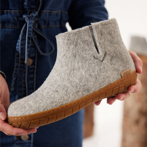Close-up picture of hands holding a lGrey glerups boot with a natural rubber sole.